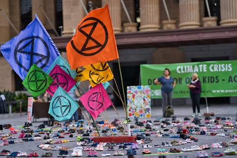 Demonstração do Extinction Rebellion com bandeiras coloridas e umaexposição de sapatos decriança